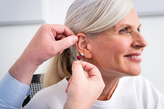 Ältere Frau bekommt ein modernes Hörgerät eingesetzt, Hörakustiker berät freundlich.